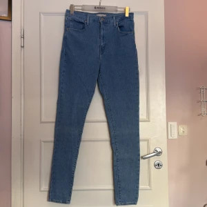 Blå jeans Mile High Super Skinny från Levi's - Säljer ett par snygga blå Mile High Super Skinny jeans från Levi's. De är högmidjade med en tight passform och klassisk femficksdesign. Perfekta för en stilren look. Är väldigt stretchiga och sköna att ha på sig, har knappt använt