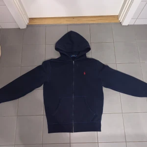Mörkblå hoodie från Ralph Lauren - Säljer en snygg mörkblå hoodie från Ralph Lauren med dragkedja och det klassiska röda logotypen på bröstet. Storlek XS. Perfekt skick