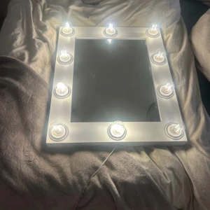 Sminkspegel med lampor original pris1200kr - Säljer en stilren sminkspegel med inbyggda lampor runt ramen. Perfekt för att få bra belysning vid sminkning eller styling. Spegeln har en vit ram och kan enkelt placeras på ett bord eller hängas upp på väggen. Lamporna ger ett jämnt och klart ljus.
