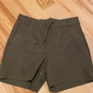 Olivgröna shorts från ONLY - Snygga olivgröna shorts från ONLY med elastisk midja och snörning. Perfekta för en avslappnad stil. Shortsen har två sidofickor. Riktigt snygga men tyvärr för små för mig. 