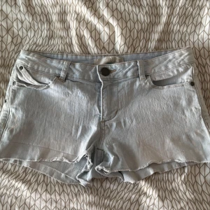 Lågmidjade jeansshorts (intressekoll) - Säljer ett par ljusblå jeansshorts med fransiga kanter. De är i bra skick men har lite fläckar på sidan som inte alls märks och ser ut att passa in i designen, jag vet inte om det är meningen. En av fickorna på baksidan är nersydd men är fullt funktionell fortfarande! Köp helst inte direkt utan skriv till mig!