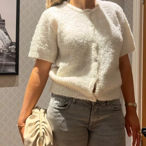 Vit fluffig kofta - Säljer en supermjuk och fluffig vit kofta med korta ärmar och knappar framtill. Perfekt för en mysig och stilren look. Passar bra till jeans eller kjol för en avslappnad stil. En liten smink fläck som lätt går bort i tvätten(sista bilden)