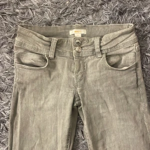 Grå jeans från Gina Tricot - Snygga grå jeans från Gina Tricot med två knappar och dragkedja fram till. Perfekta för en stilren look. Bootcut och low waisted. Storlek 146💕