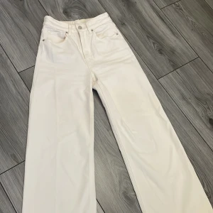 Krämvita jeansbyxor från H&M - Snygga vita jeansbyxor från H&M med en klassisk design. Byxorna har en hög midja och raka ben. Perfekta för en avslappnad men ändå chic stil. 