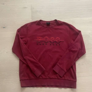 Hugo Boss - Storlek S .Säljer en vinröd sweatshirt från Hugo Boss med broderad logga på framsidan. Tröjan har långa ärmar och en rund halsringning. Perfekt för en avslappnad och trendig look.
