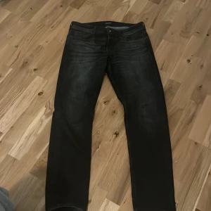 Svarta jeans från Jack & Jones - Snygga svarta jeans från Jack & Jones med en tapered passform. Modellen heter Mike och har en klassisk design med fem fickor och knappgylf. Perfekta för en stilren look. 31w 32L