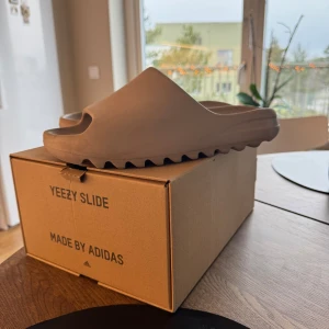 Beige Yeezy Slide från Adidas - Säljer ett par stilrena och bekväma Yeezy Slide från Adidas i en neutral beige färg. Dessa slides har en modern design med öppen tå och en räfflad sula för extra grepp. Perfekta för en avslappnad stil.