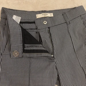 Rutig byxa från Mango - Snygga svartvita rutiga byxor från Mango med dragkedja och knapp framtill. Byxorna har en klassisk passform och är perfekta för en stilren look. De har också fickor baktill för extra funktionalitet.