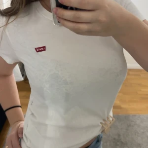 Vit t-shirt från Levi's - Säljer en klassisk vit t-shirt från Levi's med den ikoniska röda loggan på bröstet. T-shirten har en normal passform och är kortärmad, perfekt för en avslappnad stil. Finaste T-shirten och kommer ej till användning  ❤️❤️❤️🙏🏽💞☀️☀️