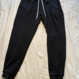 Svarta mjukisbyxor från Yoke - Säljer ett par svarta mjukisbyxor från Yoke med snörning i midjan och ribbade muddar vid bensluten. Byxorna har en bakficka och är perfekta för en avslappnad stil.