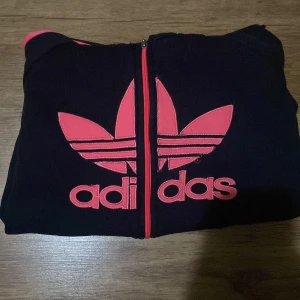 Svart och rosa hoodie från Adidas - Svart hoodie från Adidas med rosa detaljer och dragkedja.