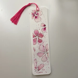 Handgjord bokmärke med blommotiv - Unikt handgjort bokmärke med vackra rosa blommor i akvarellstil. Bokmärket har en rosa tofs som ger en extra touch av elegans. Perfekt för att hålla koll på var du är i din favoritbok. Tofsen går självklart att byta färg på hör bara av er!