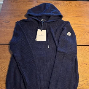 Mörkblå stickad tröja från Moncler - Säljer en snygg mörkblå stickad tröja från Moncler. Den är stickad med en ribbad struktur.Moncler-logga på ärmen ger en exklusiv touch. En tröja som man inte ser så ofta.Tröjan är i jättebra skick. Tröjan är storlek L, är det något du undrar eller om du vill ha fler bilder så är det bara att du hör av dig!