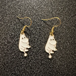 Guldiga Mumin-örhängen - Charmiga örhängen med Mumin-motiv i guld. Perfekta för Mumin-fans som vill ha något unikt och lekfullt i sin smyckessamling. Hängande design med krokfäste.