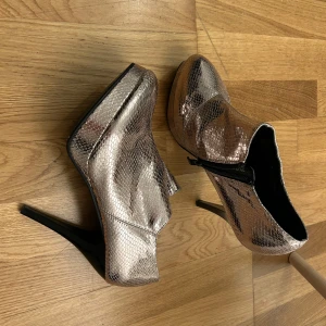 Glittriga klackskor med dragkedja - Snygga glittriga klackskor från Unisa i en metallisk nyans. Skorna har en spetsig tå och en praktisk dragkedja på sidan för enkel på- och avtagning. Perfekta för att ge en extra touch till din outfit.