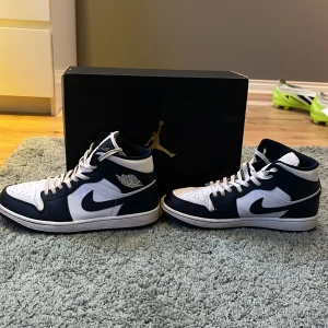 Nike Air Jordans White gold metallic obsidian  - Snygga Nike Air Jordans i mörkblå och vitt med klassisk snörning. Perfekta för dig som älskar stilrena sneakers med ikonisk design. Skorna har en perforerad tå för extra ventilation. Hör av dig vid minsta fundering.