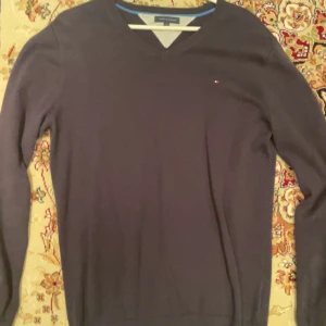 Mörkblå tröja från Tommy Hilfiger - Säljer en stilren mörkblå tröja från Tommy Hilfiger med v-ringning. Tröjan har långa ärmar och en liten logga på bröstet. Perfekt för en klassisk look.