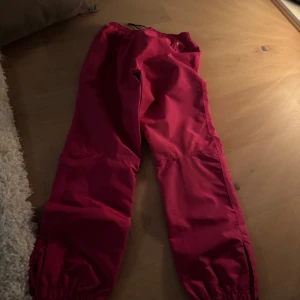 Röd vindjacka med huva + byxor  - Säljer en röd vindjacka som funkar mot regn men oxå skidåkning med huva + byxor till. 