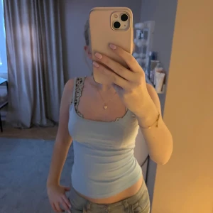 Ljusblå linnetopp med spetsdetaljer - Säljer en ljusblå linnetopp med spetsdetaljer vid axlarna. Toppen är ärmlös och har en tight passform, perfekt för sommardagar.