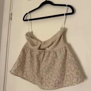 Beige axelbandslös topp med blommönster - Söt beige axelbandslös topp med stickad överdel och blommigt mönster på kjoldelen. Perfekt för varma sommardagar eller en avslappnad utflykt. Den har smala axelband och en luftig passform.