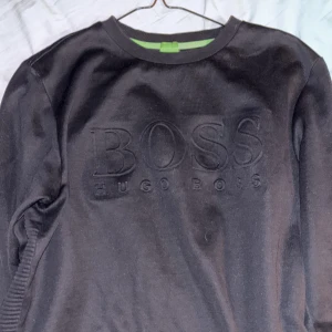 Svart tröja från Hugo Boss - Snygg svart tröja från Hugo Boss med diskret logga i relief på framsidan. Tröjan har en slim fit passform och är perfekt för en stilren look. Den har långa ärmar och en rund halsringning.