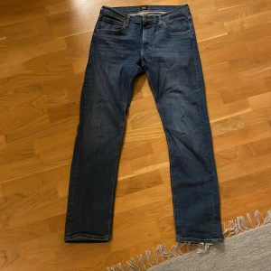 Blå jeansbyxor från Lee - Snygga blå jeansbyxor från Lee med klassisk femficksdesign. Byxorna har en normal passform och är perfekta för en avslappnad stil. De har en dragkedja och knapp framtill.