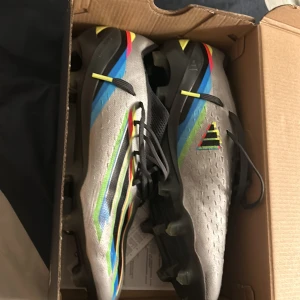 Fotbollsskor från Adidas - Snygga fotbollsskor i silver med färgglada detaljer i blått, rött och gult. Skorna har snörning och en modern design som passar perfekt för fotbollsplanen. Fotbolls skorna kostar 3000 kr nya 