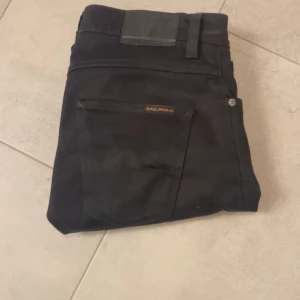 Svarta jeans från Nudie Jeans modell grim tim  - Snygga svarta jeans från Nudie med en go passform. De har en klassisk design med fem fickor och en diskret logga på bakfickan. Perfekta för en stilren look. Ett måste i garderoben! (W30 L32) tveka inte att skriva om minsta fundering