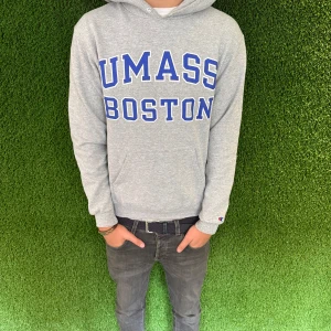 Hoddie college  - Säljer en grå hoodie från Champion med blått UMass Boston-tryck på framsidan. Tröjan har en klassisk passform med långa ärmar och en bekväm huva. Perfekt för en avslappnad stil.