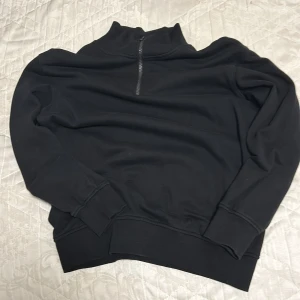 Svart tröja med dragkedja - Snygg svart tröja med halv dragkedja och hög krage. Perfekt för kyligare dagar. Tröjan har långa ärmar och ribbade muddar vid ärmslut och nederkant.