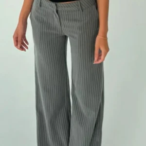 Grå randiga kostymbyxor från Venderby's - Snygga ljusgrå kostymbyxor från Venderby's med vita ränder. Byxorna har en klassisk design med låg midja och vida ben. Byxorna är aldrig använda och skickas i originalförpackningen.