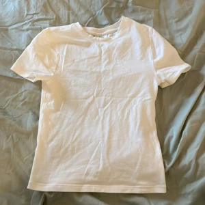 Vit t-shirt från H&M Divided - Säljer en klassisk vit t-shirt från H&M Divided. Perfekt basplagg med korta ärmar och rund hals. Enkel och stilren design som passar till det mesta. Perfekt för lager-på-lager eller som den är.