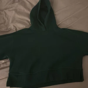 Mörkgrön croppad hoodie - Säljer en mörkgrön croppad hoodie med en bekväm passform. Hoodien har en stor huva och ribbade kanter vid nederkanten. Hoodien är i storlek M men brukar vanligtvis ha xs/s