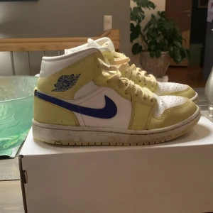 Nike Air Jordans i gult och blått - Snygga Nike Air Jordans i en fräsch kombination av gult och blått. Skorna har en klassisk hög design med snörning och en vit bas. Perfekta för dig som vill ha en stilren och sportig look.