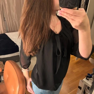 Svart blus från ONLY - Säljer en elegant svart blus från ONLY i storlek 36. Blusen har långa ärmar och en fin knytning vid halsen. Materialet är lätt och något transparent, vilket ger en stilren look. Perfekt för både vardag och fest!