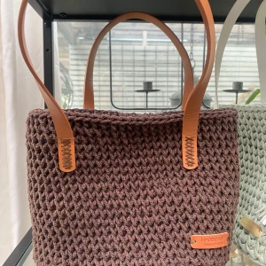 Brun stickad väska med läderdetaljer - Säljer en superfin brun virkad väska. Den har snygga läderhandtag och en stabil botten med små metallfötter. Perfekt för höstshopping eller som en chic vardagsväska. 👜
