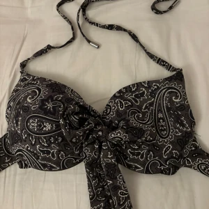 Militärgrön mönstrad bikiniöverdel - Säljer en snygg militär grön bikiniöverdel med ett coolt paisleymönster. Den har knytband i nacken och en knytning framtill. Perfekt för sommarens alla stranddagar!