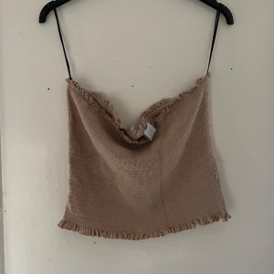 Beige ribbad linnetopp från H&M - Säljer en superfin beige ribbad linnetopp från H&M. Den har tunna axelband och en söt volangdetalj längs kanten. Perfekt för sommardagar eller att styla med en kavaj för en chic look. Toppen är i storlek XL och i nyskick.