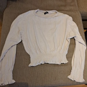 Vit långärmad topp med resårdetaljer - Säljer en superfin vit topp med långa ärmar. Den har en elastisk midja och ärmslut som ger en snygg passform. Perfekt för både vardag och fest! 💫