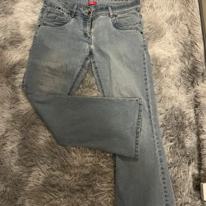 Lågmidjade, bootcut jeans i ljusblå - Säljer ett par lågmidjade ljusblå bootcut/straight vintage jeans i bra skick. Storleken på lappen är 14 petit, motsvarar cirka en L fast med kortare längd, där med petit. De har en klassisk femficksdesign med snygga broderier på bakfickorna. 