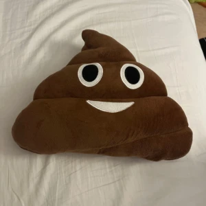 Kudde formad som en bajs emoji - Säljer en rolig och mjuk brun kudde formad som en bajs emoji med ett glatt ansikte. Perfekt för att liva upp soffan eller sängen med lite humor. Kudden är i nyskick och gjord av mjukt material som är skönt.