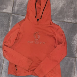 Funktionell hoodie - Orange hoodie med 2 st fickor med dragkedja. Har blivit lite fläckig efter tvätt av någon anledning. 