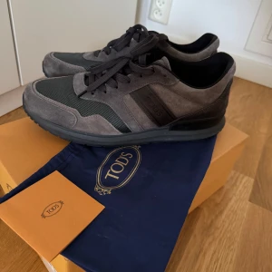 Grå sneakers från Tod's - Säljer ett par snygga grå bruna sneakers från Tod's i nyskick. Skorna har en stilren design med mockadetaljer. De har en klassisk snörning och är superbekväma. Perfekt för höst vinter. Nypris 375 euro. Säljer för 1495. Storlek 10 passar 44/45