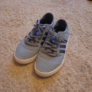 Blå sneakers från Adidas - Säljer ett par snygga blå sneakers från Adidas. De har de klassiska tre ränderna på sidan och är i bra skick. Perfekta för vardagsbruk och passar till nästan allt. Skorna har snörning och en vit sula som ger en fräsch look. Lite små i stl. 
