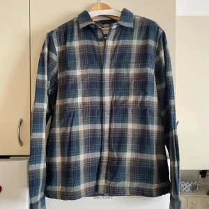 Rutig skjorta från East West - Säljer ny RELAXED FIT OVERSHIRT från East West i storlek M. Skjortan är i blå och grå toner med ett klassiskt rutmönster. Den är långärmad och tillverkad i 100% bomull, Perfekt för hösten, den är tjockare men mjuk och skön   