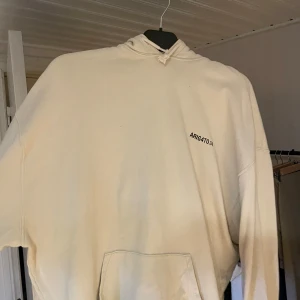 Beige hoodie från Axel Arigato - Säljer en snygg beige hoodie från Axel Arigato med tryck både fram och bak. Den är i storlek L och har en klassisk känguruficka framtill. Perfekt för en avslappnad stil och passar till alla årstider. Huvan har dragsko för justerbar passform. Skicka ett meddelande vid intresse!