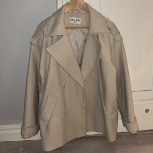 Kort kappa NAKD - Kort kappa från nakd i beige, artikelnummer 1100-007227-0260. Storlek 38.  Använd en gång så väldigt bra skick. Säljer för 600kr.   Kan mötas upp i Gbg annars står köparen för frakten. Köpt är köpt 😊