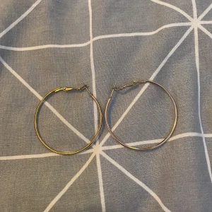 Guldiga hoop-örhängen - Säljer ett par stilrena guldiga hoop-örhängen. De är stora och perfekta för att ge en elegant touch till vilken outfit som helst. Passar både till vardags och fest. Lätta att bära och stängs med en enkel låsmekanism.