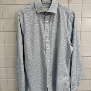 Ljusblå rutig skjorta från GANT i Tech Prep – Storlek M - Superfin ljusblå skjorta från GANT med rutigt mönster i det funktionella Tech Prep-materialet. Storlek M och i mycket fint skick.