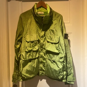 Grön jacka från Stone Island - Säljer en grön jacka från Stone Island i glänsande material. Den har långa ärmar och flera praktiska fickor framtill. Perfekt för höst och vår. Passar både till vardags och fest!
